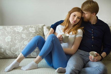 美丽的年轻夫妇男孩和红头发的女孩坐在沙发上喝茶照片