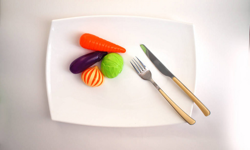 儿童的人造蔬菜, 叉子和小刀, 躺在白色的背景白色的盘子上