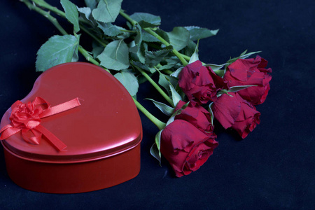 一束鲜红的玫瑰和一颗心形的盒子里的礼物。五朵花躺在黑色的表面上