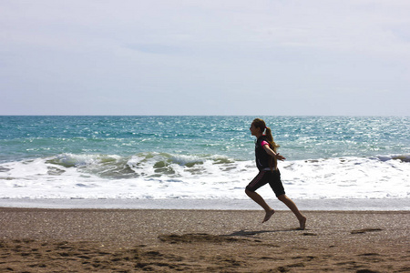 年轻女孩奔跑和跳跃在海滩在蓝色海附近