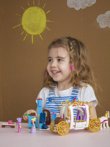 可爱有趣的学前儿童小女孩玩建筑玩具积木建设一个塔在幼儿园房间。由太阳和云彩描绘的背景
