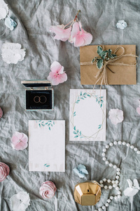 婚礼请柬, 信封, 戒指, 装饰和粉红色的花蕾在灰色毯子上。新娘平躺, 顶视图概念