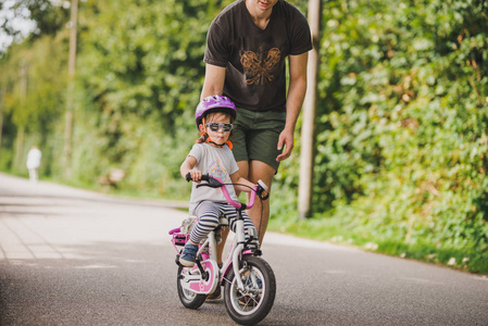 父亲教小孩子女儿骑自行车在公园里