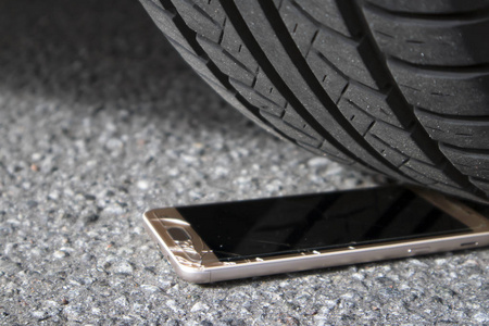 现代智能手机与裂纹的屏幕玻璃在沥青下的汽车车轮