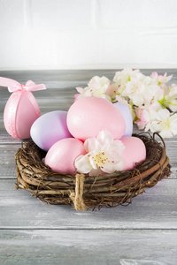 完美的彩色手工复活节彩蛋在一个巢与春天的花朵在一个木灰色的背景。复活节快乐
