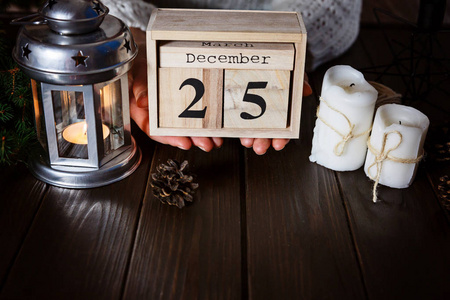女人手持有木制日历与12月25日日期在黑暗的木质背景。新年和圣诞节的概念, 装饰品