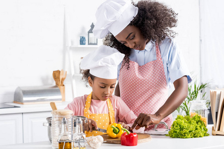 非洲裔美国人的母亲和女儿在厨师帽子切开菜在厨房