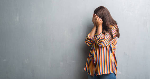 年轻的褐发女郎女人在垃圾灰色墙壁与悲伤的表情覆盖脸与手一边哭。抑郁症概念