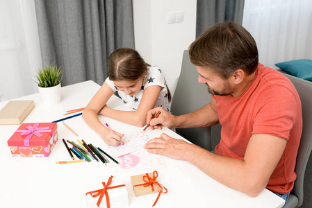 高角度肖像的大胡子父亲帮助小女孩画手工贺卡为母亲节在家中的现代客厅