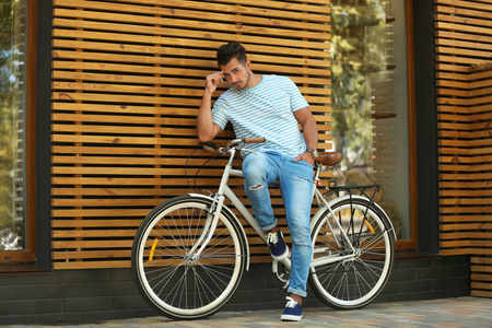 英俊的年轻时髦男子与自行车附近的木墙户外