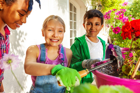 幸福的朋友, 多民族的男孩和女孩的肖像, 在阳光明媚的日子用花园铲的盆栽植物