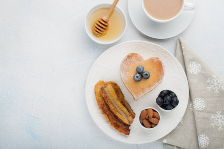 一堆美味的煎饼与蜂蜜, 咖啡和蓝莓在淡蓝色背景。情人节的早餐很丰盛。具有复制空间的顶部视图