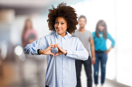 在背景模糊的人做心脏符号的年轻黑人妇女