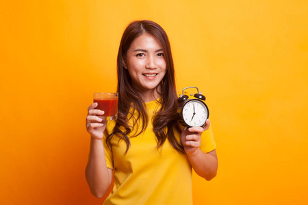 年轻的亚洲妇女与蕃茄汁和时钟在黄色礼服