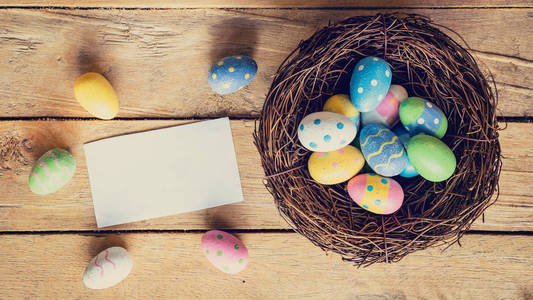 五颜六色的复活节彩蛋在巢和纸卡片在木头背景
