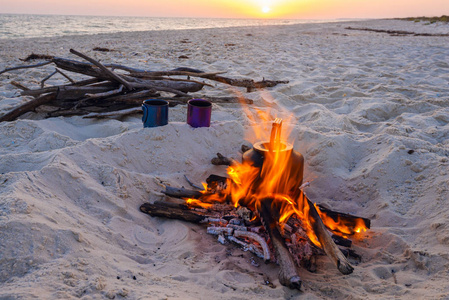 在海上日落时, 两个杯子站在篝火旁。