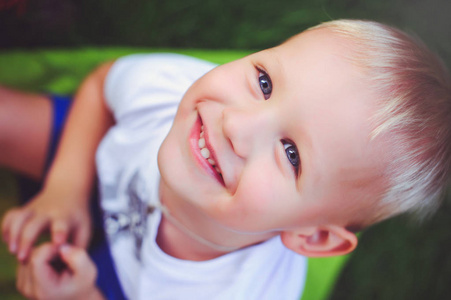 快乐的蓝眼睛金发男孩看着相机微笑着。柔和的暖色调