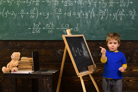 一个狡猾的脸站在绿色板前面的小男孩。瞳孔指向黑板。儿童学习算术