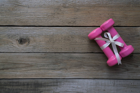 两个粉红色哑铃与白色礼物弓在木桌背景上