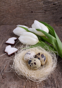 花组成与白色郁金香, 巢与鹌鹑蛋和釉状饼干形状的兔子在木桌上
