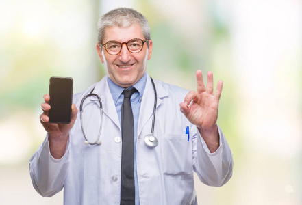 英俊的资深医生男子显示屏幕上的 smarpthone 在孤立的背景做 ok 符号与手指, 优秀的符号