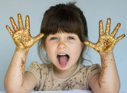 滑稽的孩子的画像显示她的手画在金子和显示舌头, 蓝色背景