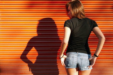 美丽的年轻女子, 长棕色的头发穿着黑色 t恤站在橙色的墙壁背景上的街道上