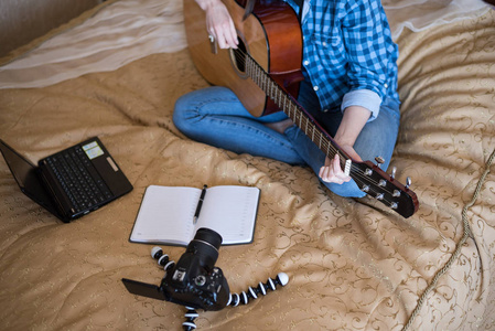 特写女孩在床上随意的衣服演奏声学吉他和写博客在单反相机