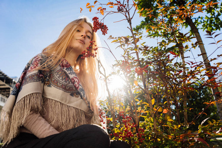迷人的年轻金发女孩坐在太阳旁边的树