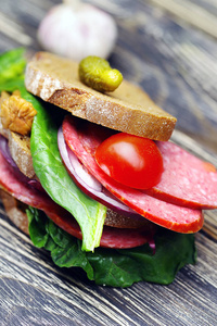 一个大的新鲜的三明治与意大利香肠和蔬菜在一个黑暗的木桌