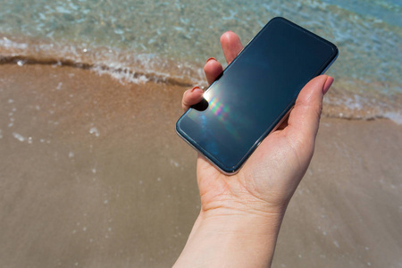 美丽的女人的手在海滩使用智能手机