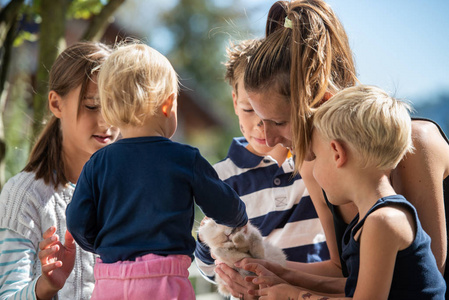 年轻的母亲与四孩子在外面阳光明媚的一天拥抱他们毛茸茸的宠物兔子