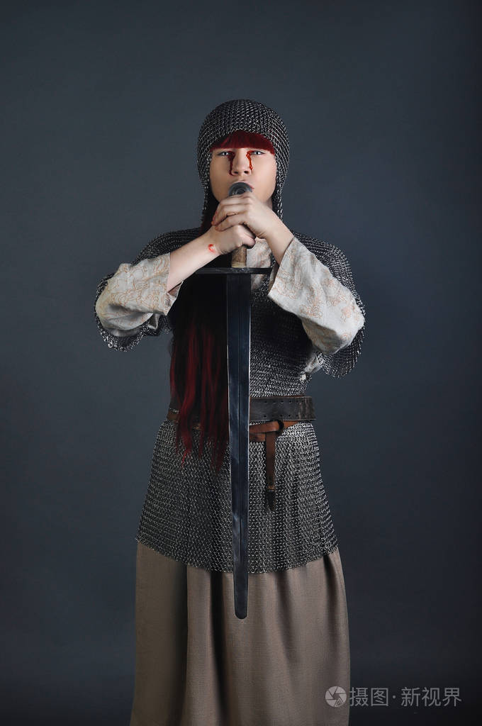 中世纪女孩在链邮件与红头发的剑站在灰色的背景与她的手上的血