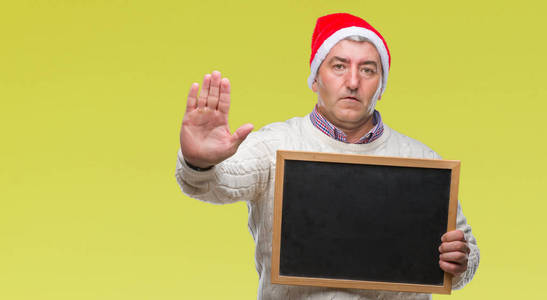 英俊的老人戴着圣诞帽子和持有黑板在孤立的背景与开放的手做停止标志与严肃和自信的表达, 防御手势