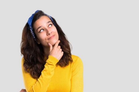 年轻的女孩与黄色毛衣和蓝色头巾在她的头站立和思考孤立灰色背景的想法