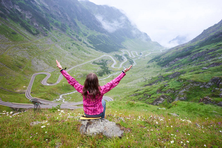 一个快乐的女性旅行者的后视镜观看 Transfagarasan 路坐在草地上的小山上与她的双臂分享快乐旅游旅游