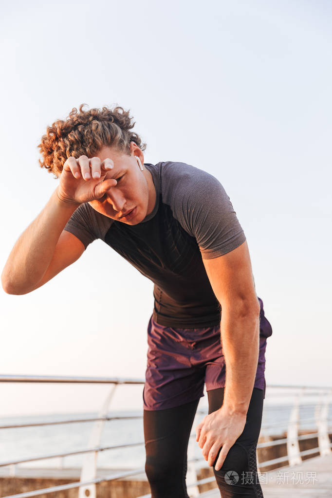 在海滩锻炼后休息的出汗运动员的肖像, 听音乐与耳机照片-正版商用