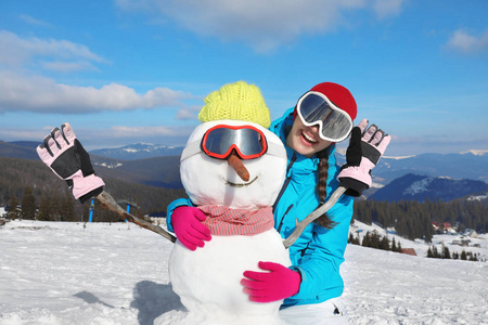 快乐的女人与雪人在度假胜地。寒假