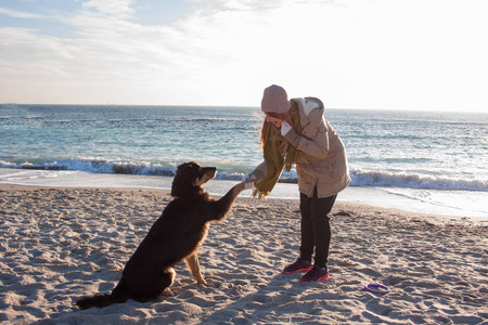 阳光明媚的日子, 年轻女子在沙滩上与大黑狗玩耍