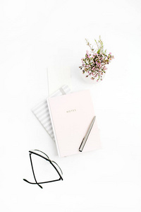女性家庭办公桌上有笔记本眼镜钢笔和野花的白色背景。平面放置, 顶部视图博客概念