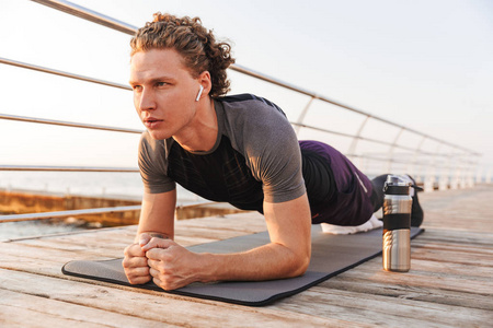 一个自信的运动员的肖像做木板运动在健身垫海滩, 听音乐与耳机