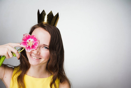 美丽的年轻女子拿着粉红色的花朵在她的脸上, 戴着金色王冠, 等待世界妇女节