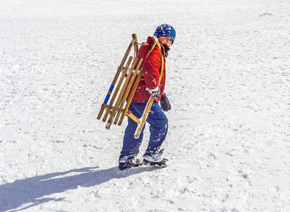 男孩运载他的雪橇在小山上图片