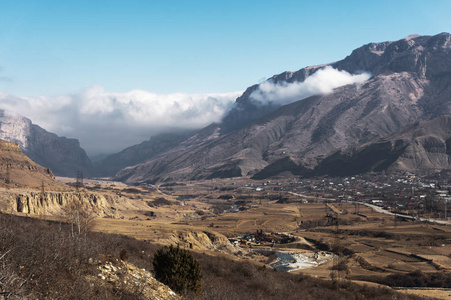 在高加索峡谷的山村的看法。有云和峡谷的山的灰色山峰与房屋和定居点