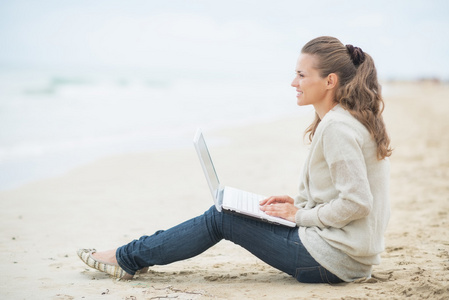 幸福的女人坐在一起的笔记本电脑在冷的海滩上