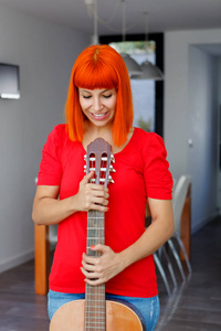 红发快乐的年轻女子与吉他在家里
