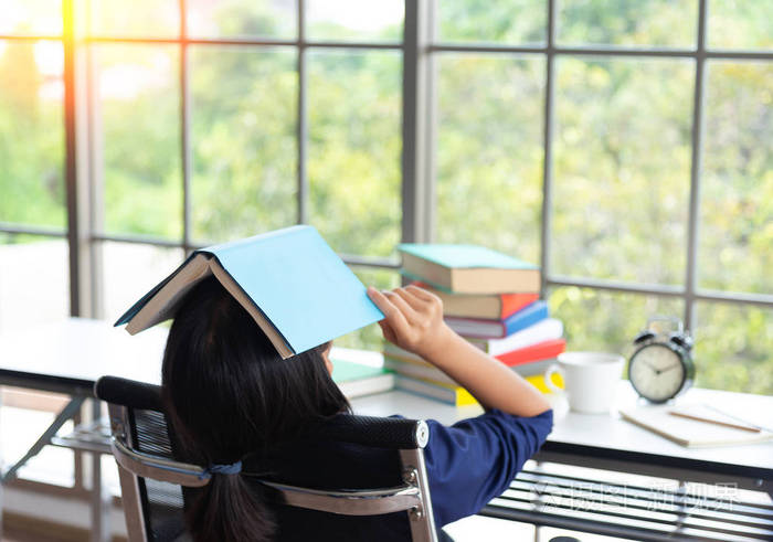 漂亮的小女孩躺在桌子上睡在一堆书里, 疲惫的学生躺在书本上睡觉