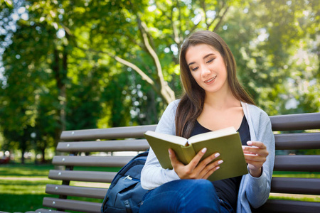 年轻的亚洲妇女坐在公园的长凳上。放松和阅读一本书