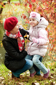 小女孩和妈妈躲在一棵树在秋天公园后面