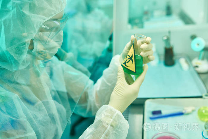 在医学研究实验室中穿着防护服和面具工作的女科学家的侧面视图画像